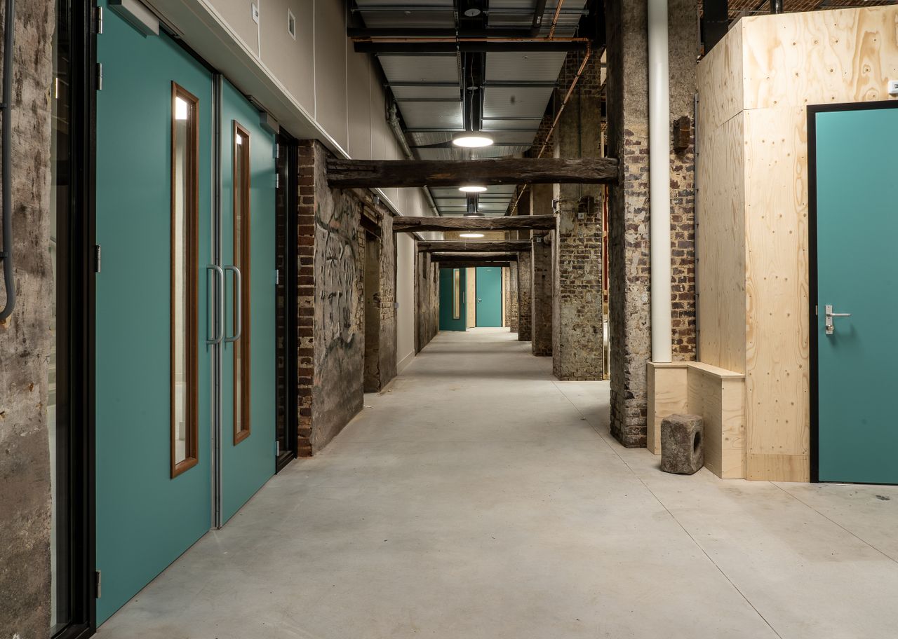 A modern industrial hallway with exposed brick and teal doors, ideal for creative spaces.